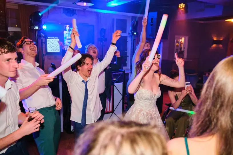 Foto van een bruiloft met dansende mensen met in hun hand een foamstick